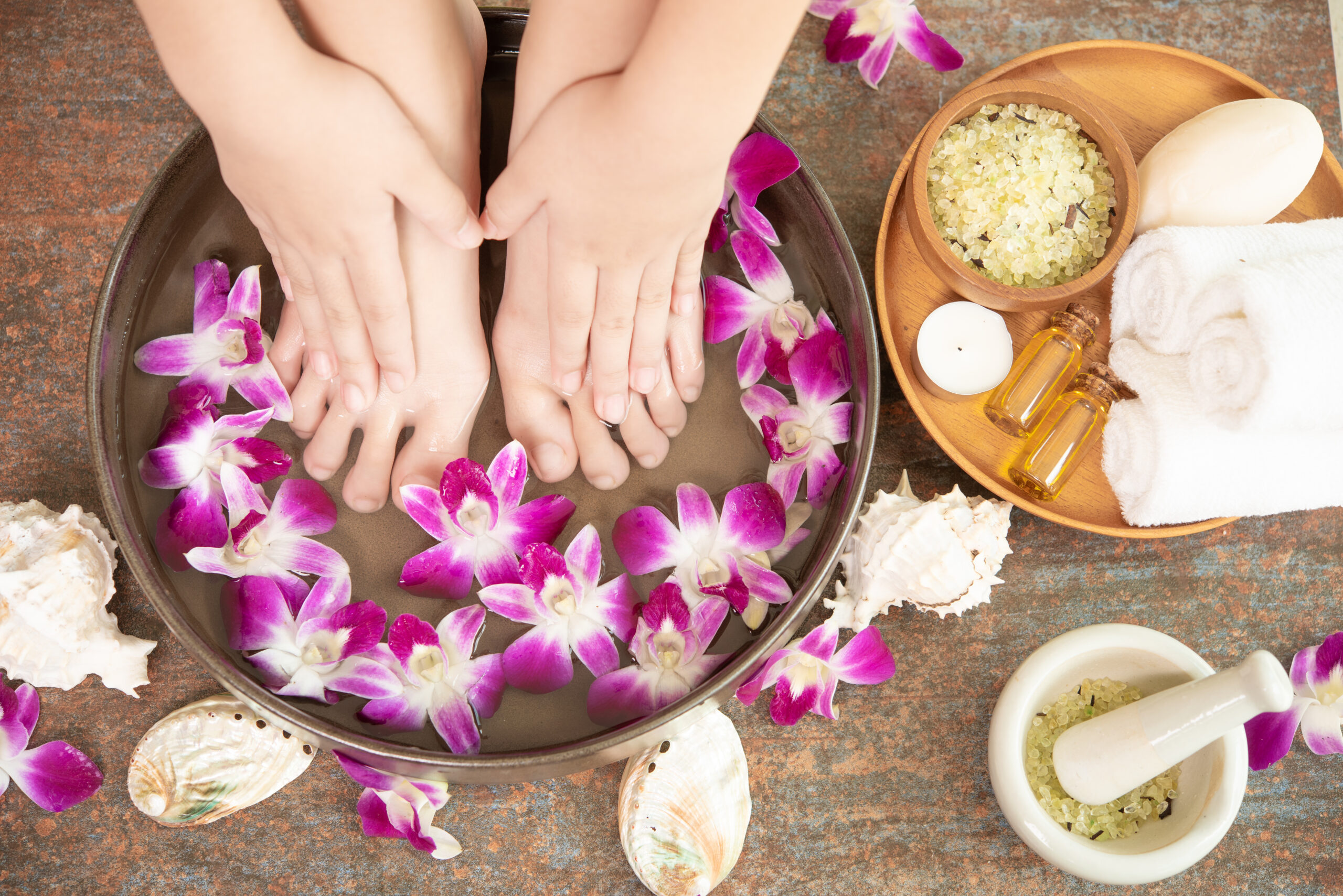 closeup view of woman soaking her hand and feet in dish with water and flowers on wooden floor. Spa treatment and product for female feet and hand spa. orchid flowers in ceramic bowl.